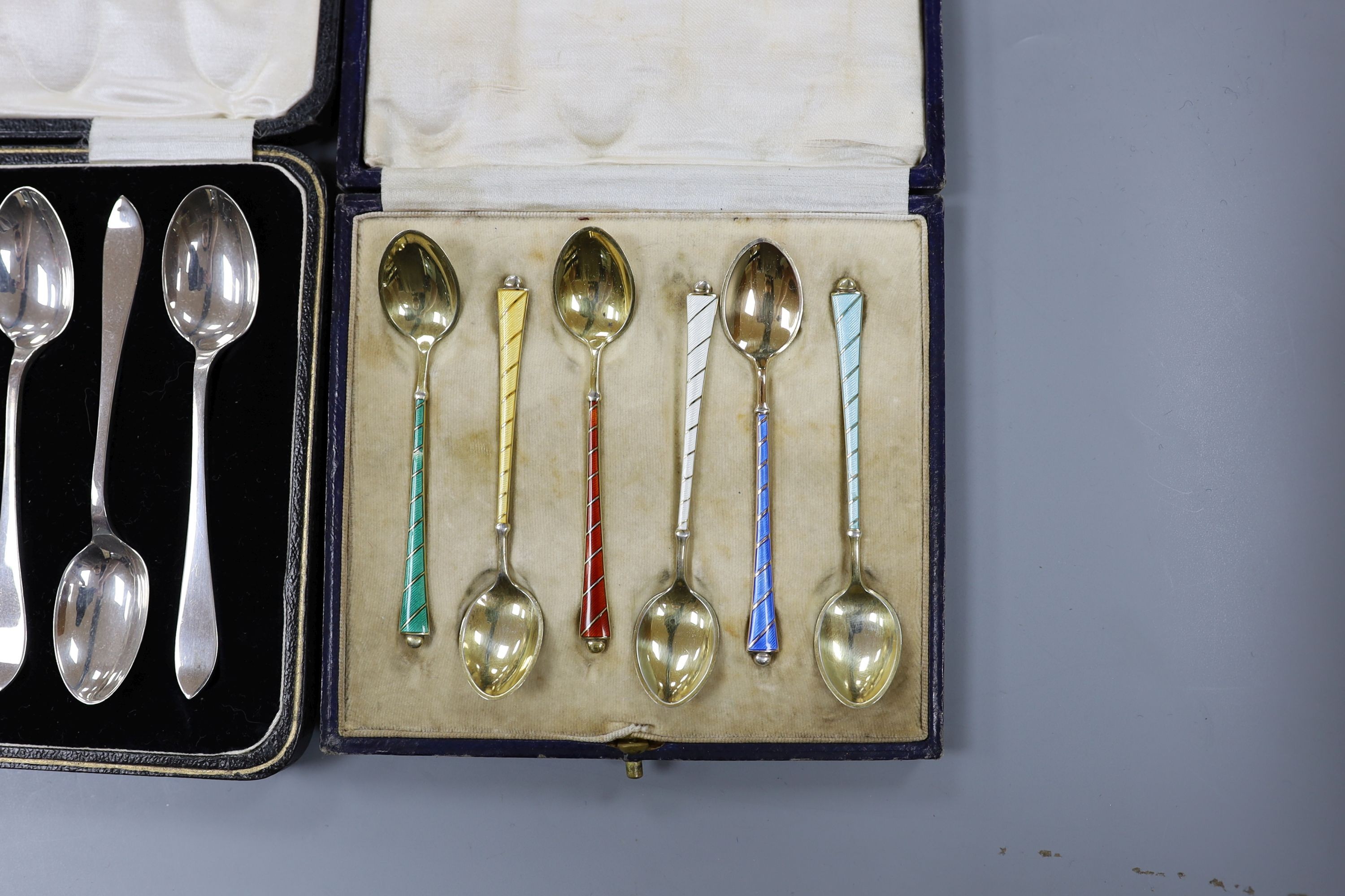 A cased set of six Danish gilt sterling and polychrome enamel coffee spoons, a cased set of six silver teaspoons with tongs and a cased set of six silver handled tea knives.